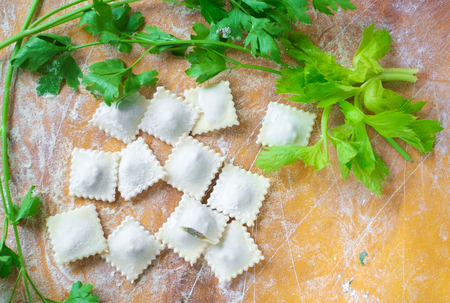 traditional raw ravioli with green and meat on a wooden table with flour, handmade, cooking process, top viewの写真素材