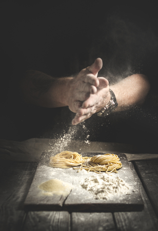 hands in flour, make homemade pasta on a table on black backgroundの写真素材