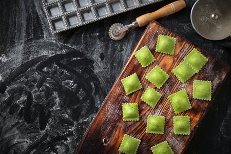 cooking green ravioli on a wooden Board on a black background with flourの写真素材
