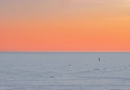 Sunset scene of a lone man figure in the distance in winter on a frozen lake