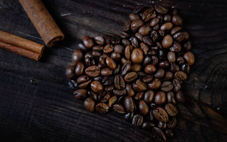Coffee beans in the form of a heart on a wooden background with a cinnamon stickの写真素材