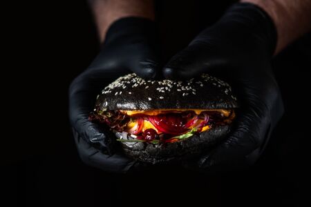 Close up of hands holding black juicy burger with cranberry sauce on dark backgroundの写真素材