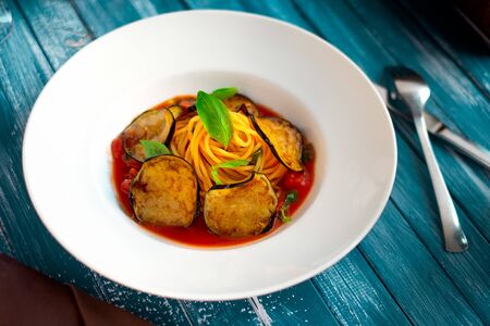 Vegetarian Spaghetti pasta with eggplants and tomato sauce on a white plate and wooden blue...