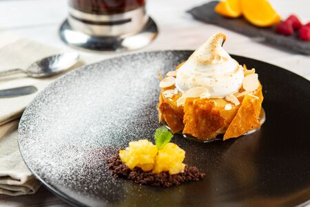 A portion of Apple pie with cream on a black plate. Charlotte dessert baked with nuts