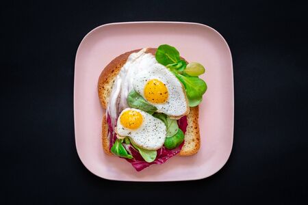 Healthy breakfast sandwiches concept. Bread toasts with fried eggs and green salad on pink plate on...