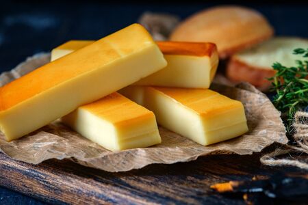 Italian smoked Mozzarella cheese sticks in paper on a wooden board on dark background, close-upの写真素材
