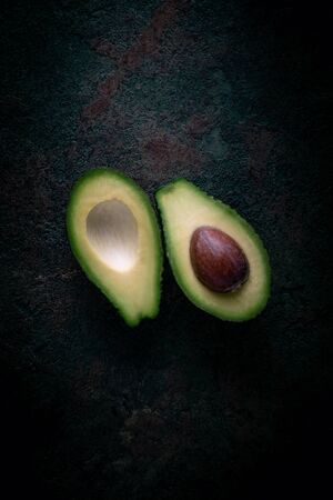 Ripe avocado cut in two on a dark stone background, top view, copy spaceの写真素材