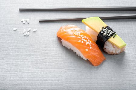 Nigiri sushi with salmon and avocado on a grey background with chopsticks, close-upの写真素材