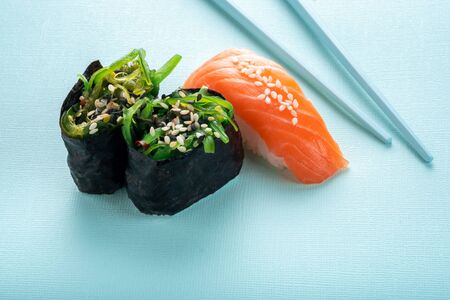 Two seaweed Sushi Chuka and sushi nigiri with salmon with chopsticks on a blue background. Copy spaceの写真素材