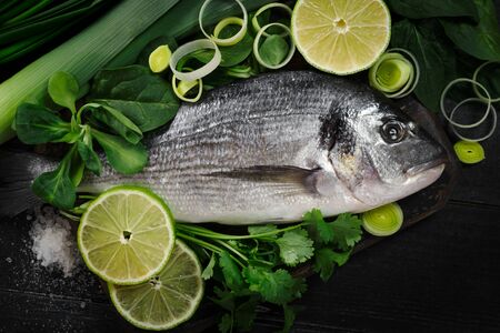 Fresh and raw dorada fish with lemon and herbs on a black wooden background, top viewの写真素材