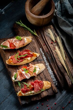 Traditional Bruschetta with Parma dried ham and prosciutto. Italian antipasti set sandwiches with jamon, cottage cheese, arugula, and sun-dried tomatoes on a rustic wooden Board, Close upの写真素材
