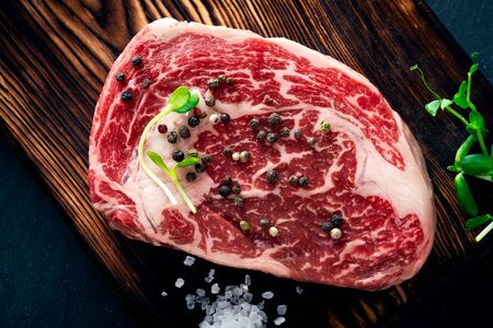 Raw rib steak from a beef with salt and pepper on wooden Board on dark background. Copy spaceの写真素材