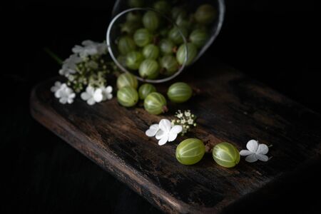 Gooseberry and flowers in glass cup on a wooden Board, still life with berries in rustic style