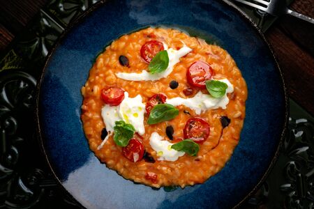 Risotto with tomatoes, Basil, cheese and olive oil on a blue plate. Italian national cuisine, rustic...