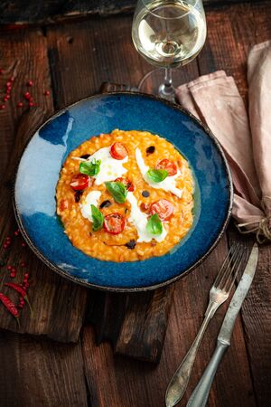 Risotto with tomatoes, Basil, cheese and olive oil on a blue plate. Italian national cuisine, rustic styleの写真素材