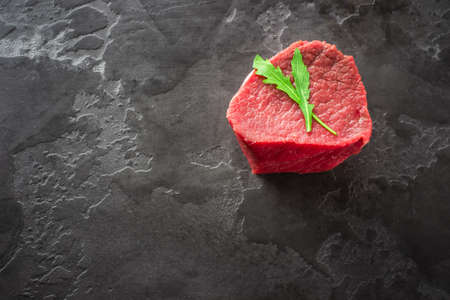 Raw beef tenderloin steak filet Mignon on a dark stone background, top view, copy space