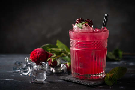 Alcoholic cocktail with blackberries, mint and ice on a dark wooden background. Refreshing red drink in a glassの写真素材