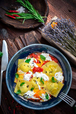 Colorful cooked ravioli with tomato, Basil and cream cheese in a plate on a wooden background. Italian pasta rustic styleの写真素材