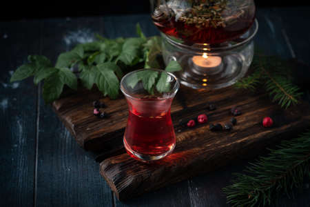 A glass of herbal tea with blackcurrants in a teapot on a dark wooden background. Fragrant natural drink from wild berries.の写真素材