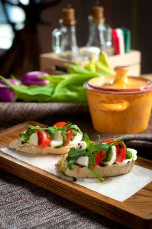 Bruschetta with tomatoes, mozzarella cheese and rocket on a old wooden board. Traditional italian...