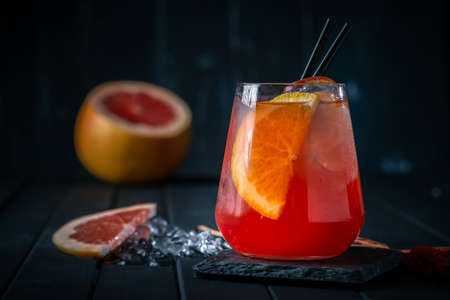 Grapefruit cocktail with Gin or vodka in a clear glass with ice on a black wooden background. Refreshing citrus lemonade, summer refreshing drinkの写真素材