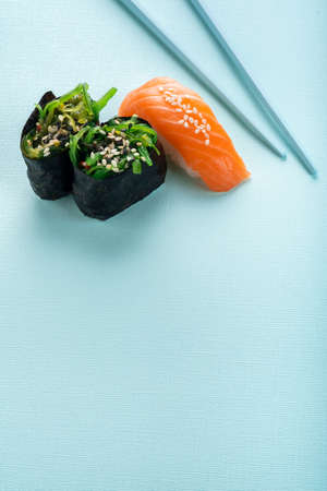 Two seaweed Sushi Chuka and sushi nigiri with salmon with chopsticks on a blue background. Copy...
