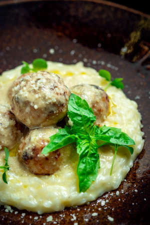 Beef meatballs with risotto in cream sauce in a plate on a wooden background. Italian cuisine rustic...