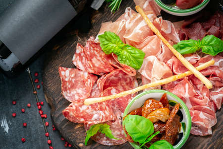 Italian meat appetizers and wine on a wooden tray. Wine snack Antipasto-salami, prosciutto, slices ham, beef jerky and bread sticks.の写真素材