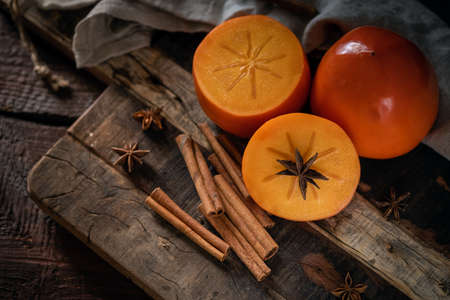 Two sliced ripe Persimmon fruit with cinnamon on old wooden table, top view