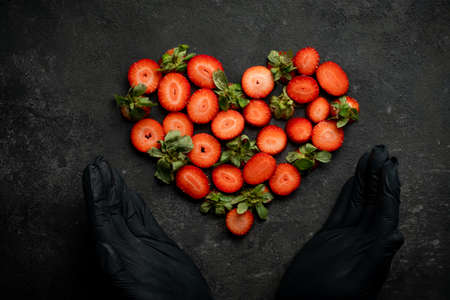 Strawberry on a dark stone background in the shape of a heart with hands, a symbol of love for Valentine's Dayの写真素材