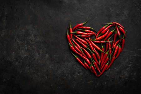 Spicy red chili pepper in the shape of a heart on a dark stone background, design concept for Valentine's dayの写真素材