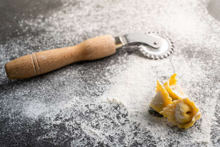 Making homemade Italian pasta ravioli with a cutting roller on stone table with flour