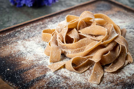 Uncooked brown pasta tagliatelle with chestnuts on a wooden Board with flourの写真素材