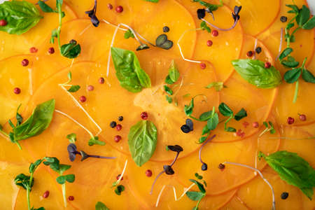 Sweet persimmon salad cut into slices with green leaves close upの写真素材