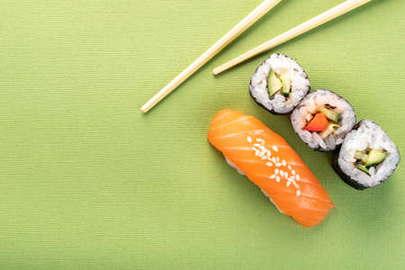 Sushi salmon nigiri and cucumber roll with chopsticks on a green background, top viewの写真素材