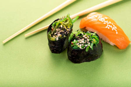 Two Chuka seaweed Sushi and salmon nigiri with chopsticks on a green backgroundの写真素材