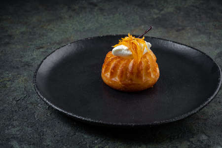 Biscuit dessert rum baba decorated with whipped cream and orange in black plate