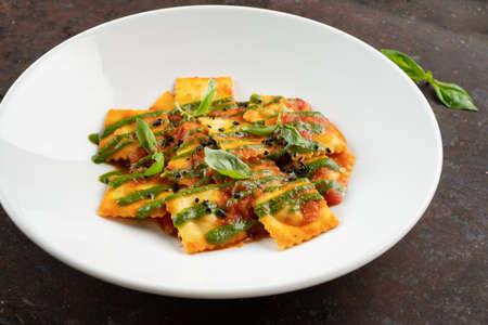 Cooked ravioli with tomatoes, pesto sauce and Basil leaves on a white plate, close-upの写真素材