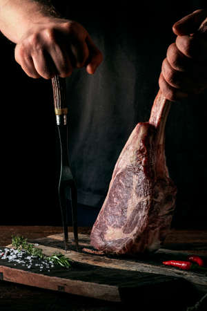 A man holds a Raw Tomahawk steak on a bone of dry aged beef on a dark backgroundの写真素材