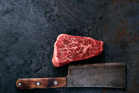 Raw marbled steak from the shoulder blade beef with a meat cleaver on a dark backgroundの写真素材