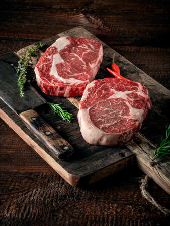 Raw rib eye steak of beef on a wooden Board with a meat cleaver and seasoningsの写真素材