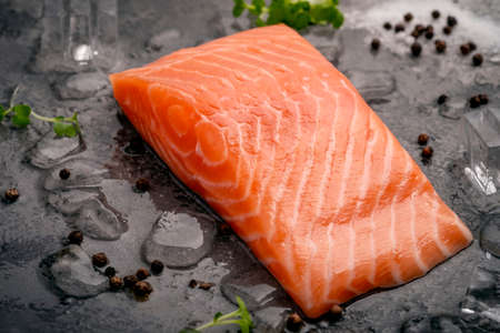 Fresh natural raw salmon fillet on ice cut into steak on a stone background with seasonings and herbsの写真素材
