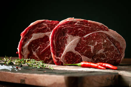 Raw rib eye beef steak with pepper and herbs on a wooden background in a butcher shopの写真素材