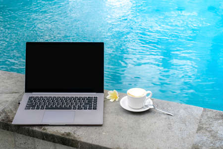 Laptop at the swimming pool with a Cup of coffee, workspace at a freelancer on vacation