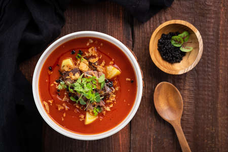 Tomato cream soup with smoked brisket and potatoes in a white bowl on a wooden background, top view and rustic styleの写真素材
