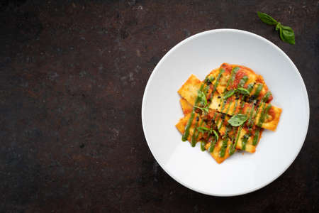 Cooked ravioli with tomatoes, pesto sauce and Basil leaves on a white plate, top view and copy spaceの写真素材