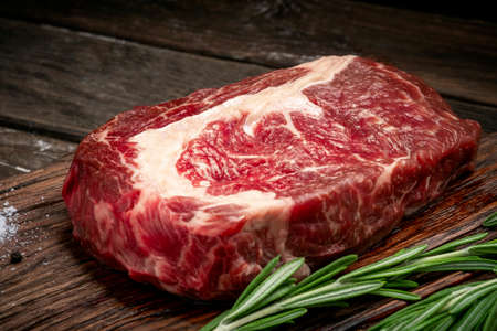 Raw rib eye steak of beef on wooden Board with rosemary and thyme on wooden backgroundの写真素材