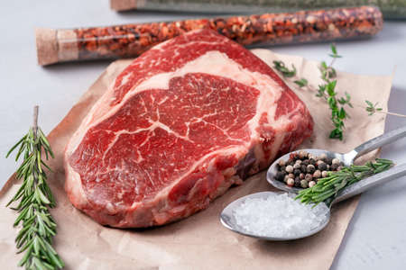Raw rib eye steak on a light background with cooking ingredients, close upの写真素材