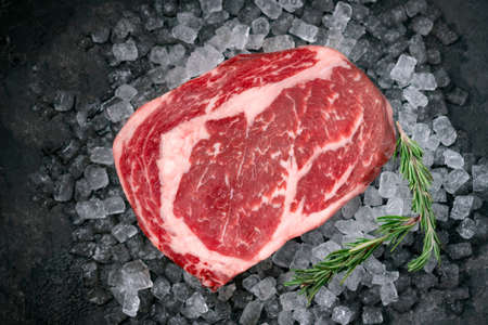 Raw fresh Rib eye beef steak on ice with herbs and rosemary, top viewの写真素材