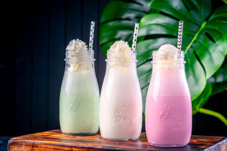 Set of different milkshakes with strawberries, mint and vanilla in glasses on a dark background with plantsの写真素材